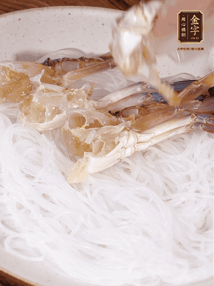 盤底墊上粉絲，擺上梭子蟹、火腿片，撒姜粒，淋上蒸魚豉油、花雕酒調(diào)味腌制15分鐘